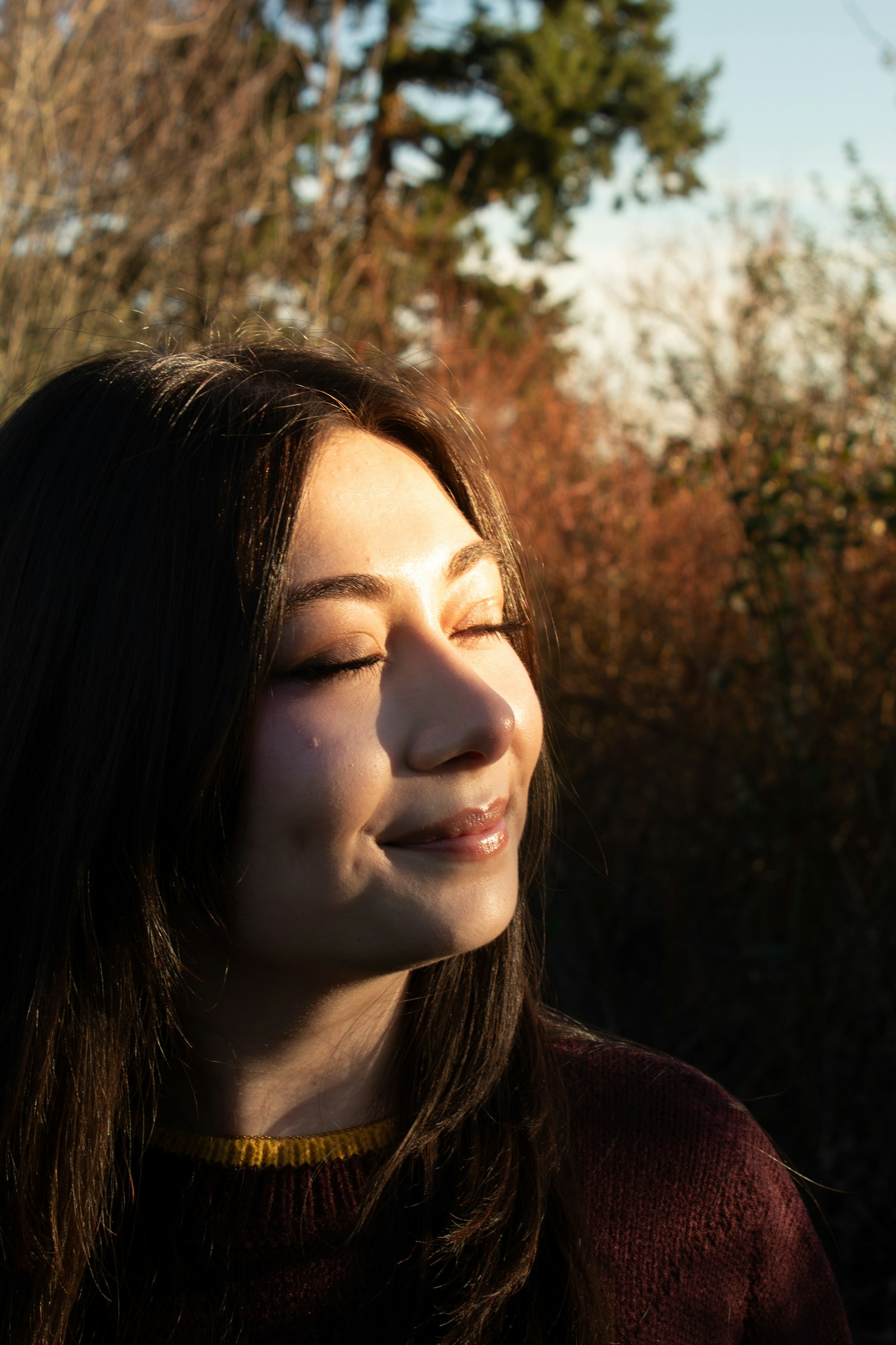Woman smiling softly with eyes closed, golden sunlight on her face