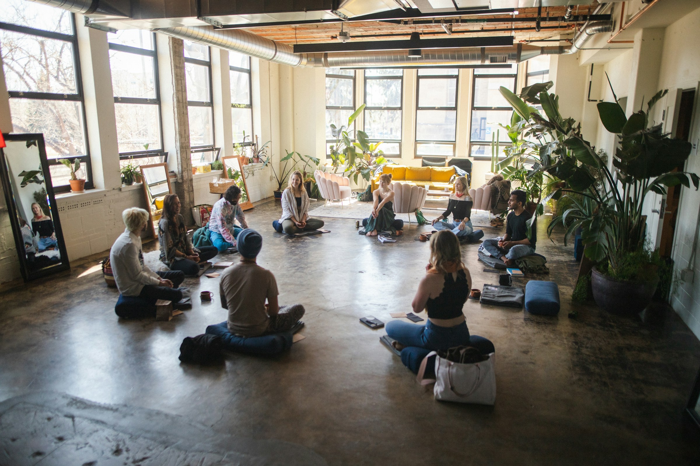 Small group seated in a circle in a bright, plant-filled studio
